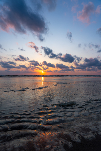 View of the sunset over Strand Wijk aan Zee with sea foam on the sandy beach and dramatic clouds Wijk aan Zee North Holland Netherlands. View of the sunset over Strand Wijk aan Zee with sea foam on the sandy beach and dramatic clouds Wijk aan Zee North Holland Netherlands.