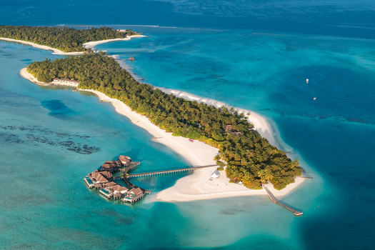 Aerial view of a tropical island resort with overwater bungalows wooden jetties white sand beaches and lush palm trees near Kudahuvadhoo Dhaalu Atoll Maldives. Aerial view of a tropical island resort with overwater bungalows wooden jetties white sand beaches and lush palm trees near Kudahuvadhoo Dhaalu Atoll Maldives.