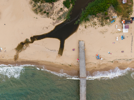 Aerial view of a concrete pier extending into the sea with a river mouth flowing onto the sandy beach small boats and people relaxing on the shore in Shkorpilovtsi Varna Bulgaria. Aerial view of a concrete pier extending into the sea with a river mouth flowing onto the sandy beach small boats and people relaxing on the shore in Shkorpilovtsi Varna Bulgaria.