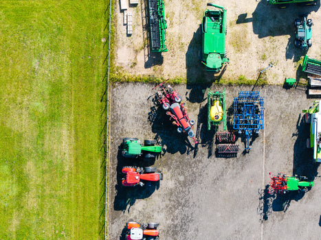 Aerial view of a farm equipment supplier yard featuring tractors harvesters and agricultural machinery parked on a paved lot adjacent to a green field in Kekava Kekava Municipality Latvia. Aerial view of a farm equipment supplier yard featuring tractors harvesters and agricultural machinery parked on a paved lot adjacent to a green field in Kekava Kekava Municipality Latvia.