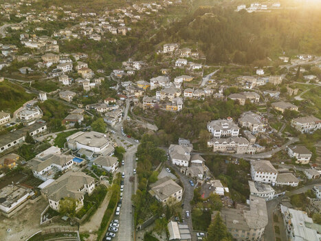 Aerial view of the historic stone houses and slate rooftops of Gjirokaster nestled on the hillside during golden hour in Gjirokaster Gjirokaster County Albania. Aerial view of the historic stone houses and slate rooftops of Gjirokaster nestled on the hillside during golden hour in Gjirokaster Gjirokaster County Albania.