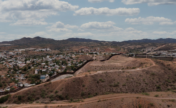Aerial view of the U.S. Mexico border wall dividing Nogales Arizona United States and Nogales Sonora Mexico across an urban desert landscape and hilly terrain.