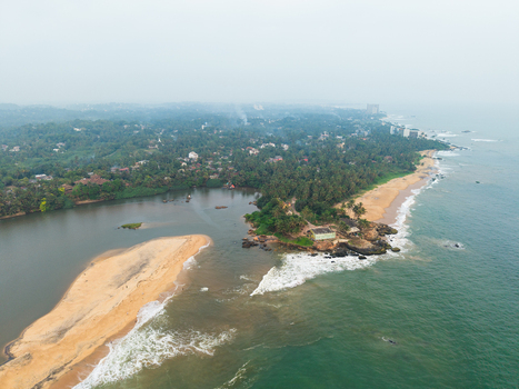 Aerial view of a river mouth meeting the ocean with sandy beaches and lush tropical palm trees in Galle Southern Province Sri Lanka.