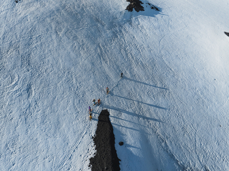 Aerial view of Mount Etna south slope with a group of hikers walking on the snow covered volcanic terrain under bright sunlight Nicolosi Sicilia Italy. Aerial view of Mount Etna south slope with a group of hikers walking on the snow covered volcanic terrain under bright sunlight Nicolosi Sicilia Italy.