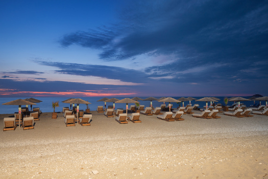 View of beach chairs and umbrellas line the sandy shore as the sky transitions from dusk to night in Kathisma Beach Kathisma Lefkada Greece. View of beach chairs and umbrellas line the sandy shore as the sky transitions from dusk to night in Kathisma Beach Kathisma Lefkada Greece.