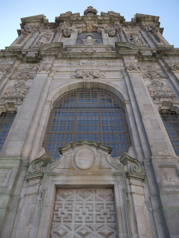 View of the ornate stone facade of the Church of Saint Ildefonso featuring intricate carvings a large arched window and a grand wooden door in Porto Porto District Portugal. View of the ornate stone facade of the Church of Saint Ildefonso featuring intricate carvings a large arched window and a grand wooden door in Porto Porto District Portugal.