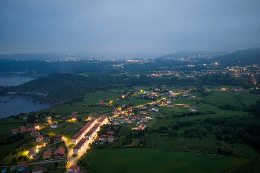 Aerial view of the illuminated village of Cudillero at dusk with glowing streetlights green fields and the dark coastline under a twilight sky in Cudillero Asturias Spain. Aerial view of the illuminated village of Cudillero at dusk with glowing streetlights green fields and the dark coastline under a twilight sky in Cudillero Asturias Spain.