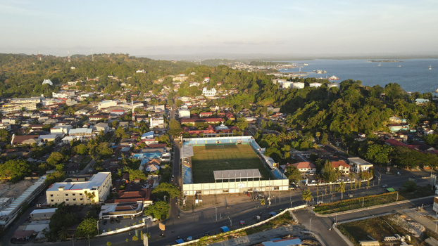 Aerial view of the city of Sorong featuring a prominent stadium surrounding urban buildings lush green hills and the coastal bay area in Sorong Southwest Papua Indonesia. Aerial view of the city of Sorong featuring a prominent stadium surrounding urban buildings lush green hills and the coastal bay area in Sorong Southwest Papua Indonesia.