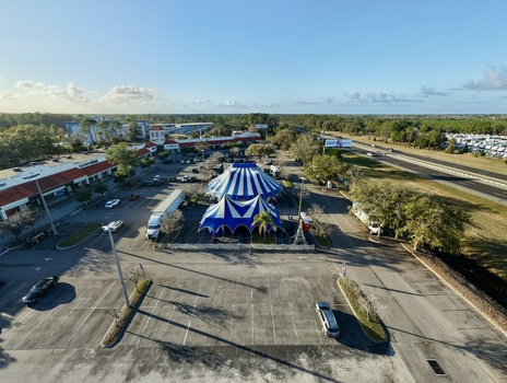 Aerial view of a vibrant blue and white circus tent standing proudly amidst a sprawling parking lot framed by lush greenery and distant buildings St. Augustine Florida United States. Aerial view of a vibrant blue and white circus tent standing proudly amidst a sprawling parking lot framed by lush greenery and distant buildings St. Augustine Florida United States.
