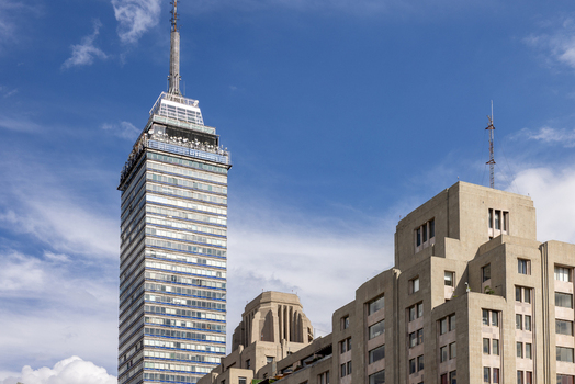 View of the Torre Latinoamericana skyscraper rising above historic stone buildings under a bright blue sky with scattered clouds in Mexico City Mexico City Mexico. View of the Torre Latinoamericana skyscraper rising above historic stone buildings under a bright blue sky with scattered clouds in Mexico City Mexico City Mexico.