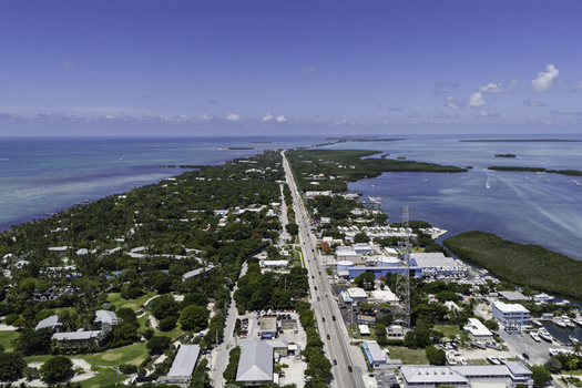 Aerial view of the Overseas Highway stretching through lush tropical vegetation surrounded by turquoise coastal waters under a clear blue sky in Islamorada Florida United States.