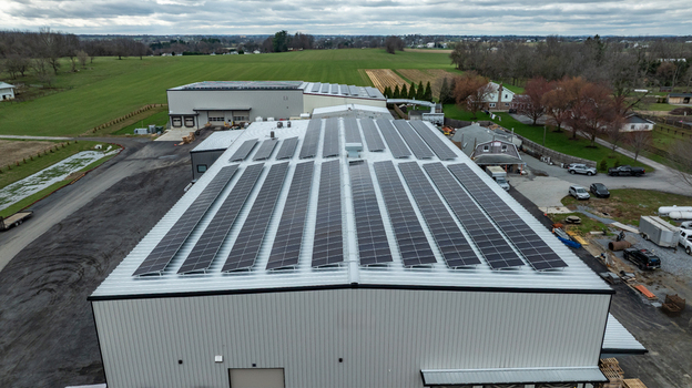 Aerial view of a large warehouse building featuring extensive solar panel arrays on its metal roof surrounded by rural fields and parking areas Gordonville Pennsylvania United States. Aerial view of a large warehouse building featuring extensive solar panel arrays on its metal roof surrounded by rural fields and parking areas Gordonville Pennsylvania United States.