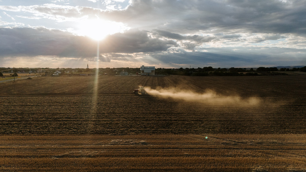 Aerial view of a tractor plowing a field and kicking up dust during golden hour in the rural landscape of Veliki Radinci Vojvodina Serbia. Aerial view of a tractor plowing a field and kicking up dust during golden hour in the rural landscape of Veliki Radinci Vojvodina Serbia.