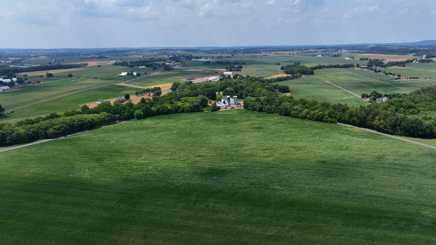 Aerial view of Salunga farmland featuring expansive green fields lush tree lines and a small farmstead with silos in Salunga Pennsylvania United States.