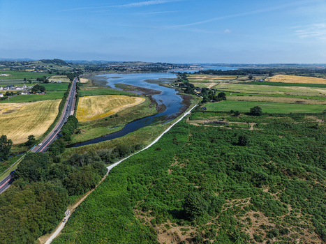 Aerial view of the winding Shimna River flowing through green fields and lush vegetation near the coast in Newcastle Northern Ireland United Kingdom. Aerial view of the winding Shimna River flowing through green fields and lush vegetation near the coast in Newcastle Northern Ireland United Kingdom.