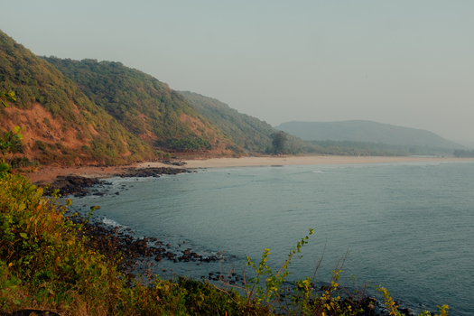 View of the tranquil beach kissed by gentle waves as lush green hills rise majestically in the distance Chiplun Maharashtra India. View of the tranquil beach kissed by gentle waves as lush green hills rise majestically in the distance Chiplun Maharashtra India.