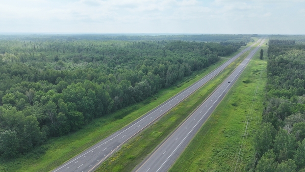Aerial view of a long highway cutting through the dense green forest with a vehicle in the distance Alberta Canada.