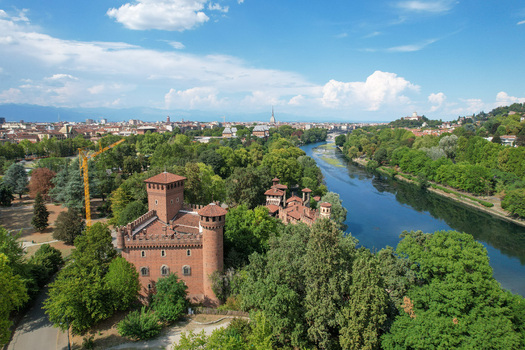 Aerial view of Borgo Medievale castle surrounded by green trees along the Po River with the city skyline in the background Torino Piemonte Italy.