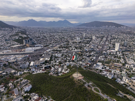 Aerial view of the Mexican flag flying atop a hill overlooking the sprawling urban landscape and mountains of Monterrey Nuevo Leon Mexico.