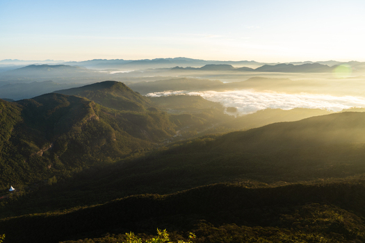 View of the misty valley and lush mountain ridges from Adam s Peak during a golden sunrise with a sea of clouds in Ratnapura Sabaragamuwa Province Sri Lanka. View of the misty valley and lush mountain ridges from Adam s Peak during a golden sunrise with a sea of clouds in Ratnapura Sabaragamuwa Province Sri Lanka.