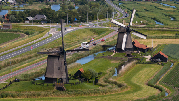 Aerial view of the historic De Museummolen windmills situated along a canal surrounded by lush green fields and a road with passing traffic in Schermerhorn Noord Holland Netherlands. Aerial view of the historic De Museummolen windmills situated along a canal surrounded by lush green fields and a road with passing traffic in Schermerhorn Noord Holland Netherlands.