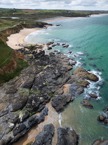 Aerial view of Godrevy Beach with dark jagged rocks sandy shores and turquoise ocean waves under a cloudy sky in Gwithian England United Kingdom. Aerial view of Godrevy Beach with dark jagged rocks sandy shores and turquoise ocean waves under a cloudy sky in Gwithian England United Kingdom.