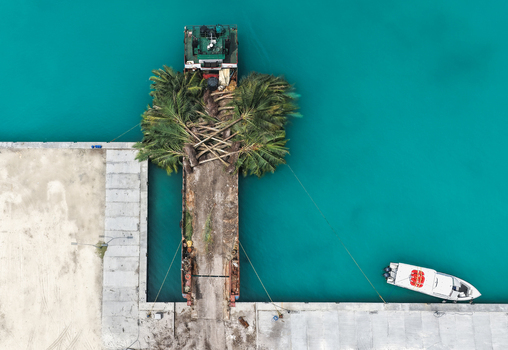 Aerial view of a cargo barge carrying palm trees docked at a concrete pier in turquoise waters Hanimaadhoo Haa Dhaalu Atoll Maldives. Aerial view of a cargo barge carrying palm trees docked at a concrete pier in turquoise waters Hanimaadhoo Haa Dhaalu Atoll Maldives.