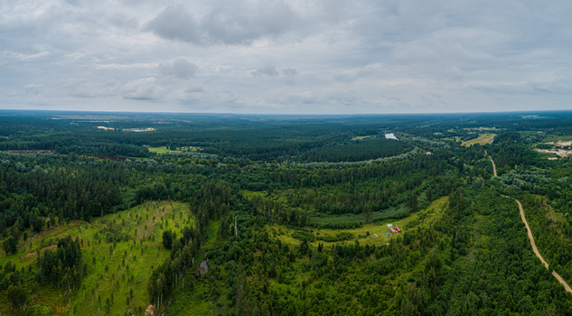 Aerial view of a vast forest landscape with a winding river dense green trees and a small campsite with tents under a cloudy sky in Latvia. Aerial view of a vast forest landscape with a winding river dense green trees and a small campsite with tents under a cloudy sky in Latvia.