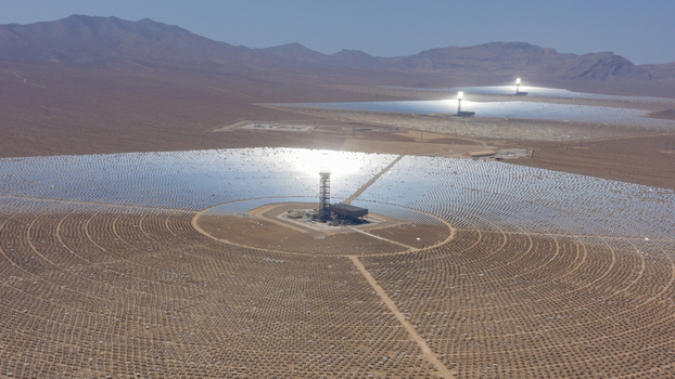 Aerial view of a concentrated solar power plant with thousands of heliostat mirrors surrounding a central solar tower in a vast desert landscape United States.