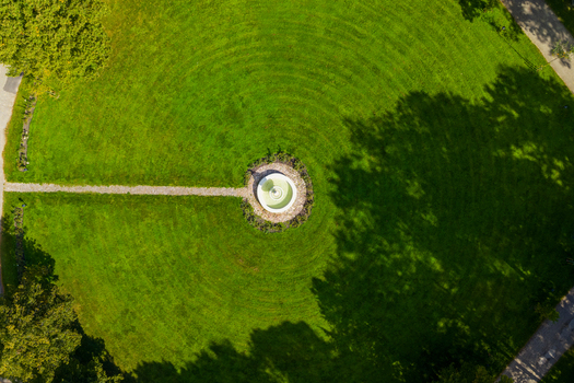 Aerial view of a circular stone fountain centered in a lush green lawn with concentric mowing patterns in Taujenai Vilnius County Lithuania.