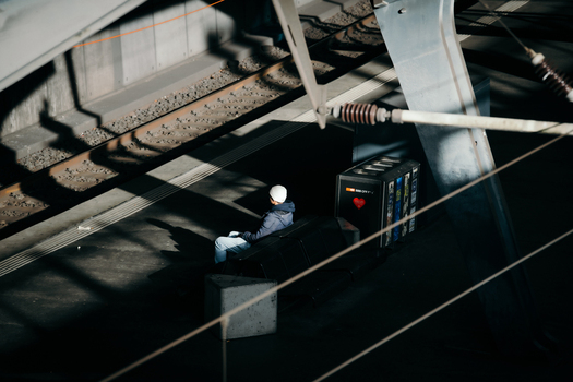 Zurich Switzerland 02 April 2023 View of a solitary figure sitting on a concrete bench bathed in stark light and shadows awaiting the train s arrival. Zurich Switzerland 02 April 2023 View of a solitary figure sitting on a concrete bench bathed in stark light and shadows awaiting the train s arrival.