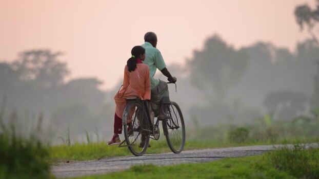 View of a man and girl riding a bicycle on a rural road Bangladesh.