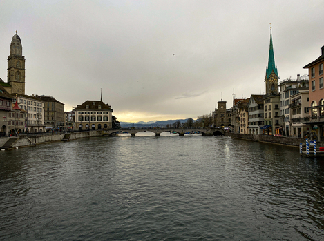 View of the Limmat river flowing through the historic city center of Zurich with the Grossmunster and Fraumunster churches under a cloudy sky in Zurich Zurich Switzerland.