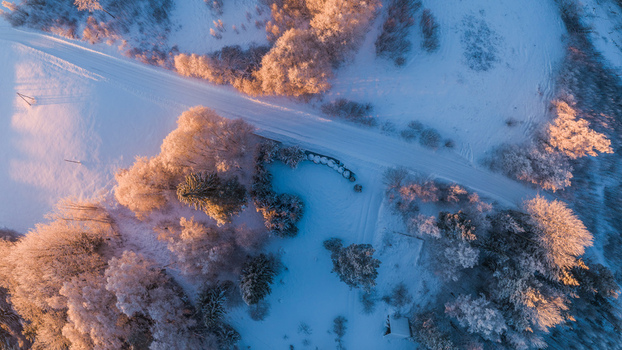 Aerial view of a snow covered landscape with a winding road and frost covered trees illuminated by the warm light of the golden hour in Latvia. Aerial view of a snow covered landscape with a winding road and frost covered trees illuminated by the warm light of the golden hour in Latvia.