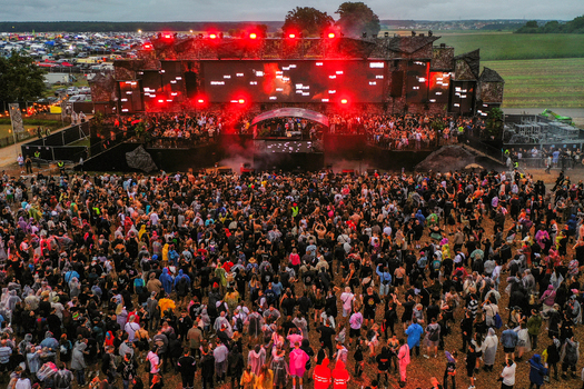 Herzogenaurach Germany 26 July 2025 Aerial view of the Open Beatz Festival with a large crowd dancing in front of a massive stage illuminated by red lights under an overcast sky.