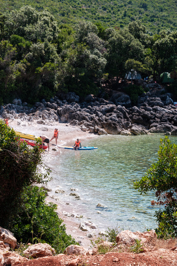Jala Albania 12 June 2026 View of Aquarium Beach with people preparing kayaks and a paddleboard on the shore surrounded by rocky cliffs and dense green forest.