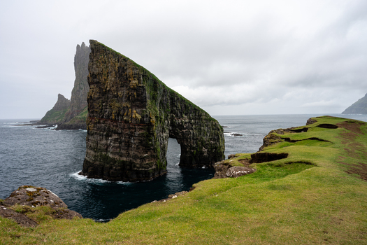 View of the Drangarnir sea stacks with a natural arch surrounded by rugged grassy cliffs and the North Atlantic Ocean in the Faroe Islands.