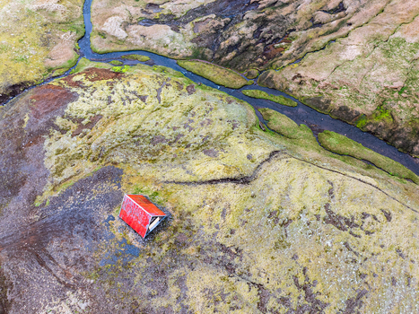 Aerial view of a small cabin with a red roof situated in a rugged mossy landscape with a winding stream in Iceland. Aerial view of a small cabin with a red roof situated in a rugged mossy landscape with a winding stream in Iceland.