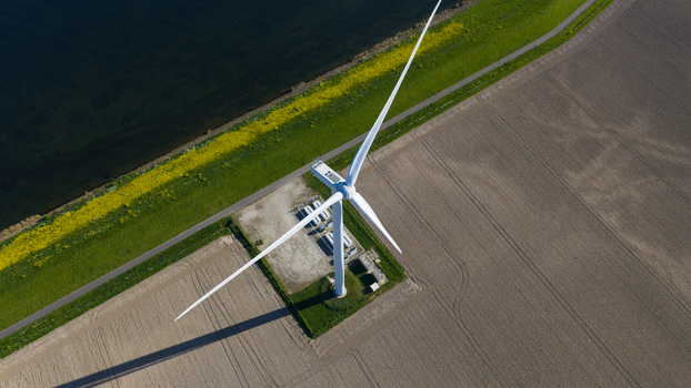 Aerial view of a modern wind turbine standing on a grassy bank between a body of water and a cultivated field in bright daylight Ooltgensplaat Zuid Holland Netherlands. Aerial view of a modern wind turbine standing on a grassy bank between a body of water and a cultivated field in bright daylight Ooltgensplaat Zuid Holland Netherlands.