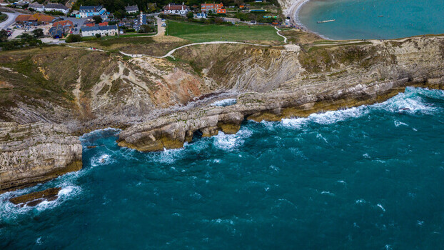 Aerial view of Lulworth Cove on the Jurassic Coast with dramatic limestone cliffs turquoise sea and coastal paths in the United Kingdom.
