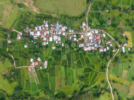 Aerial view of the rural village near Kaas plateau with vibrant green terraced rice fields small houses with metal roofs and winding dirt roads in Satara Maharashtra India.