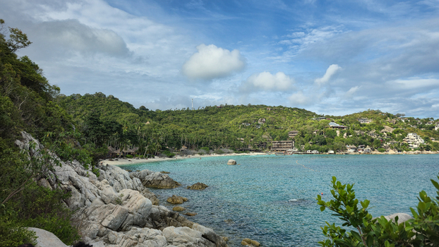 View of the coastal landscape of Ko Tao with turquoise waters rocky shoreline sandy beach and lush green hills with hillside buildings in Ko Tao Surat Thani Thailand.