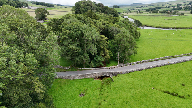 View of the Yorkshire landscape featuring a historic stone bridge over a stream surrounded by lush pastures and trees in Hawes England United Kingdom. View of the Yorkshire landscape featuring a historic stone bridge over a stream surrounded by lush pastures and trees in Hawes England United Kingdom.