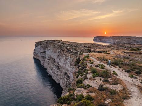 Aerial view of golden sunset paints the sky over the rugged Sanap Cliffs casting long shadows on the tranquil sea Munxar Gozo Malta. Aerial view of golden sunset paints the sky over the rugged Sanap Cliffs casting long shadows on the tranquil sea Munxar Gozo Malta.