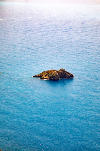 Aerial view of a small rocky islet surrounded by the clear blue waters of the Ionian Sea in Corfu Ionian Islands Greece. Aerial view of a small rocky islet surrounded by the clear blue waters of the Ionian Sea in Corfu Ionian Islands Greece.