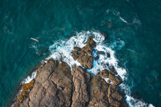 Aerial view of rocky headland with waves crashing against the shore and small fishing boats in the turquoise sea Kovalam Kerala India. Aerial view of rocky headland with waves crashing against the shore and small fishing boats in the turquoise sea Kovalam Kerala India.