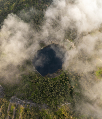 Aerial view of Kelimutu National Park crater lake surrounded by dense forest and clouds in Detusoko East Nusa Tenggara Indonesia.