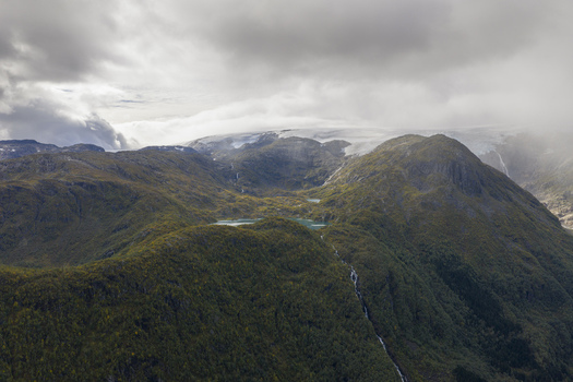 Aerial view of the Buarbreen glacier with its turquoise glacial lake lush green mountain slopes and cascading waterfalls under a cloudy sky in Ullensvang Vestland Norway. Aerial view of the Buarbreen glacier with its turquoise glacial lake lush green mountain slopes and cascading waterfalls under a cloudy sky in Ullensvang Vestland Norway.