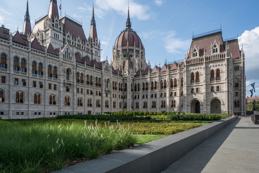 View of the Hungarian Parliament Building with its intricate Gothic Revival stone facade and green lawn in the foreground in Budapest Hungary.