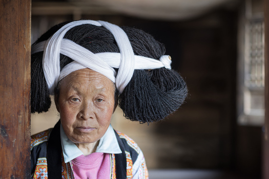 Gaoxing China 29 April 2026 View of an elderly Long Horn Miao woman wearing a traditional large hairpiece and embroidered clothing in a wooden house. Gaoxing China 29 April 2026 View of an elderly Long Horn Miao woman wearing a traditional large hairpiece and embroidered clothing in a wooden house.